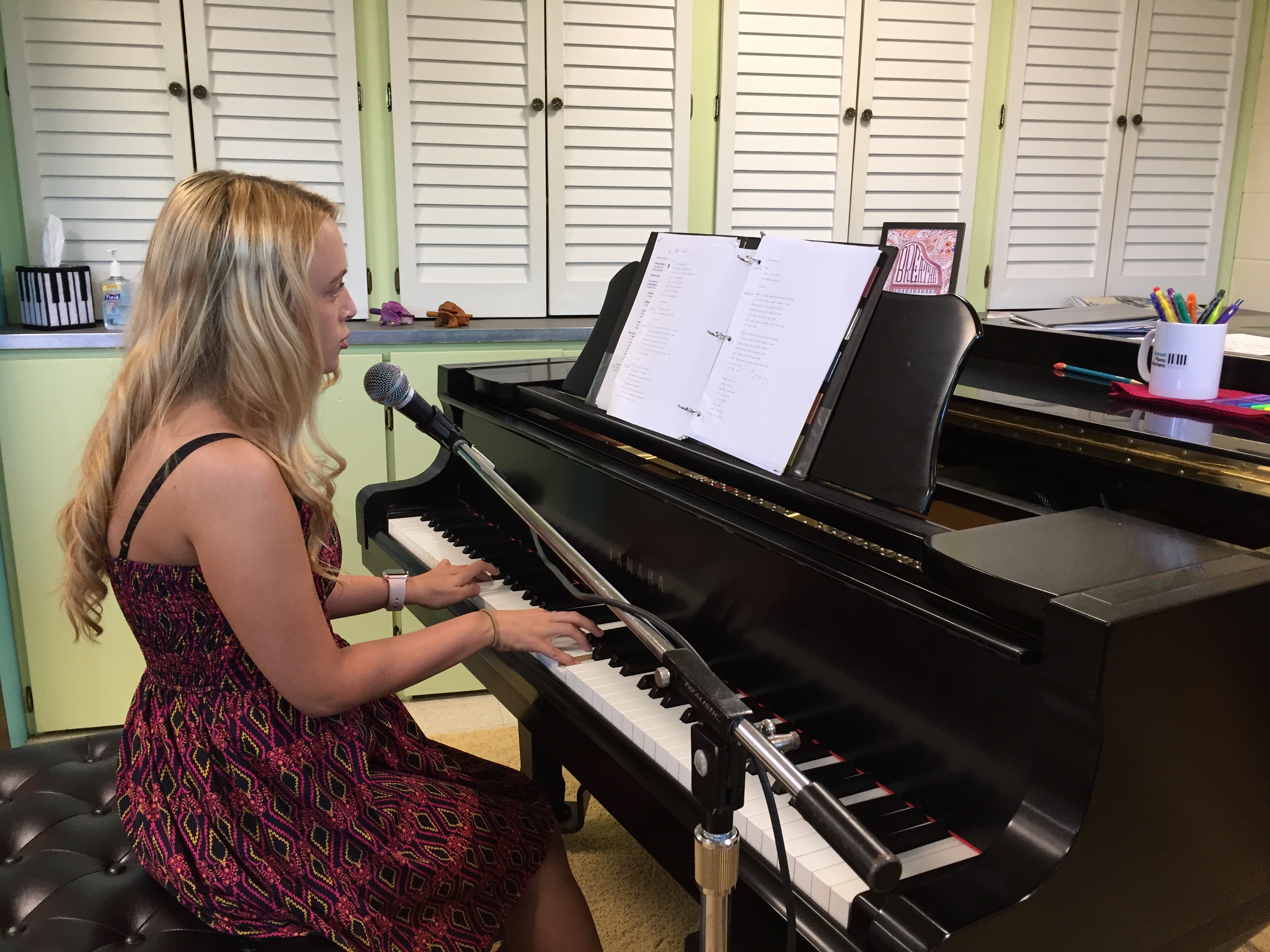 Teen girl sitting at a grand piano while playing and singing into a microphone